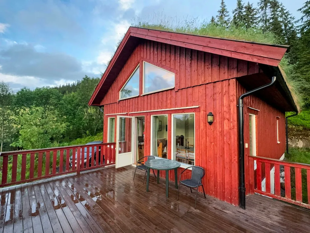 Rødmalt hytte med torvtak og stor terrasse med rekkverk i tre